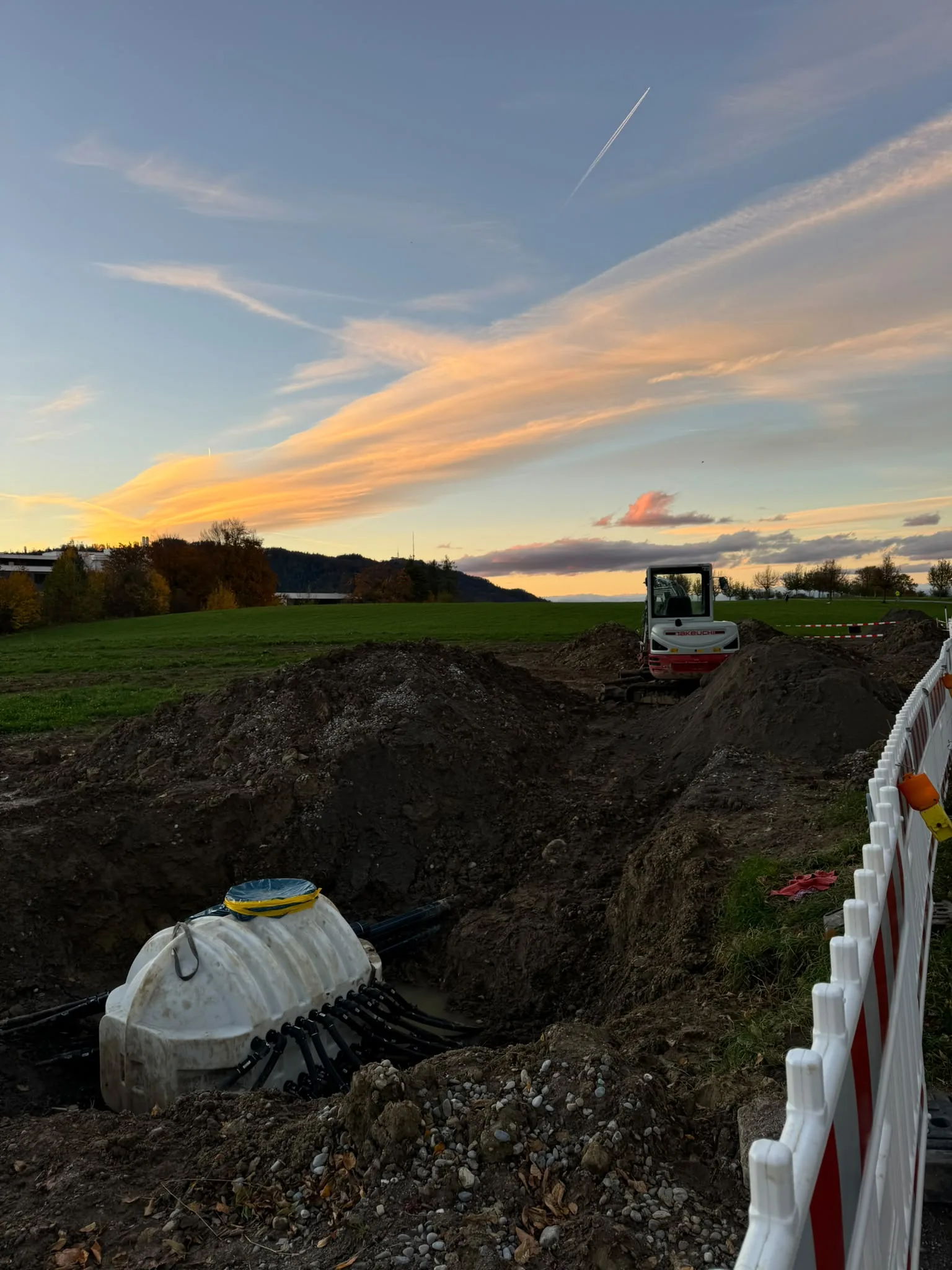 Tiefbaustelle mit Bagger auf freiem Feld im Abendlicht